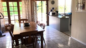 Un comedor con mesa y sillas de madera, un ventilador y vistas al jardín a través de puertas abiertas.