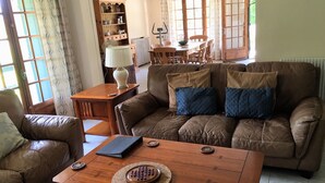 Una sala de estar acogedora con un sofá de cuero marrón, una mesa de centro de madera y una mesa de comedor con sillas.