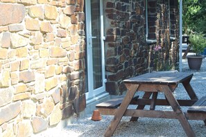 A stone building with a wooden picnic table and a potted plant. - Rural, relaxing accommodation with tranquil scenery (Redruth)