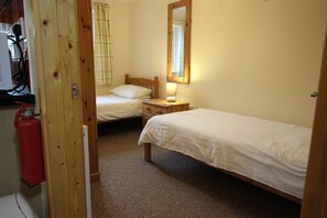 A small, cozy bedroom with two single beds, a wooden door, a bedside table with a lamp, and a mirror on the wall. - Rural, relaxing accommodation with tranquil scenery (Redruth)