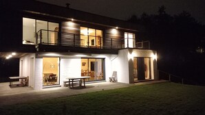 A modern two-story house with large windows, a balcony, and a well-lit entrance.