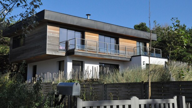 A modern two-story house with a balcony, large windows, and a wooden facade.