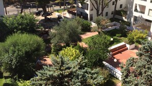 A courtyard with trees, a small building, and a view of the sea.