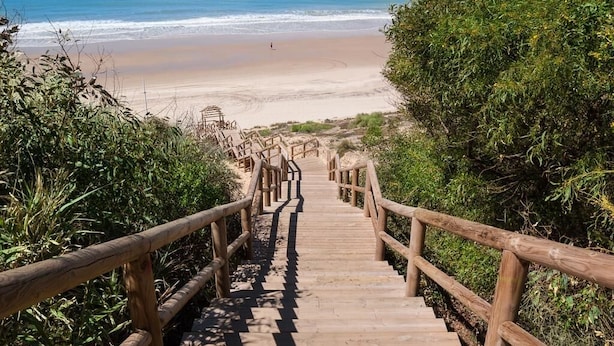 A wooden staircase leading to a beach with railings on both sides.