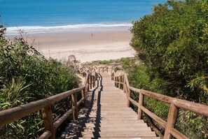 Una escalera de madera que lleva a una playa, con barandales a ambos lados.