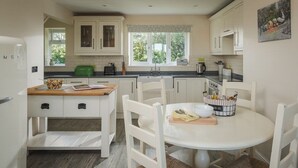 A compact kitchen with white cabinetry, a dining table, and a window with a view of greenery. - Apple Cottage - sleeps 4 guests  in 0 bedrooms (Shepton Mallet)