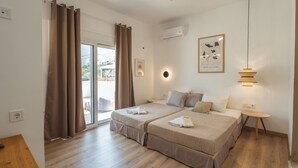 A bedroom with two beds, a ceiling fan, an air conditioning unit, a small round table, and a framed picture on the wall. - Sea-esta Beach House, Beachfront Residence & BBQ (Rethymno)