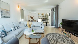 A modern living room with a sofa, coffee table, TV, and a patterned rug. - Sea-esta Beach House, Beachfront Residence & BBQ (Rethymno)