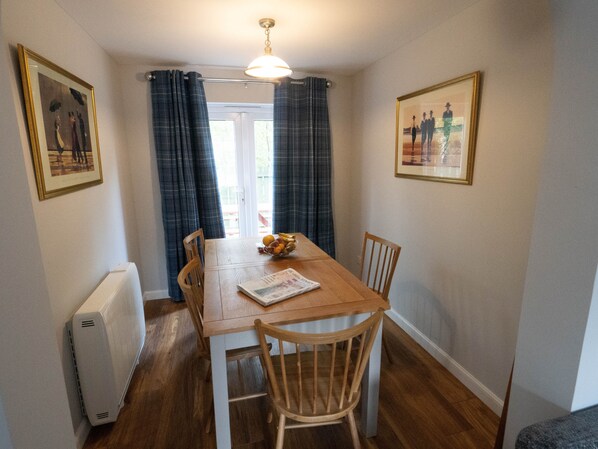 A dining area with a wooden table, four chairs, a bowl of fruit, and two framed pictures on the walls. - AVIEMORE HOLIDAY HOME (Aviemore)