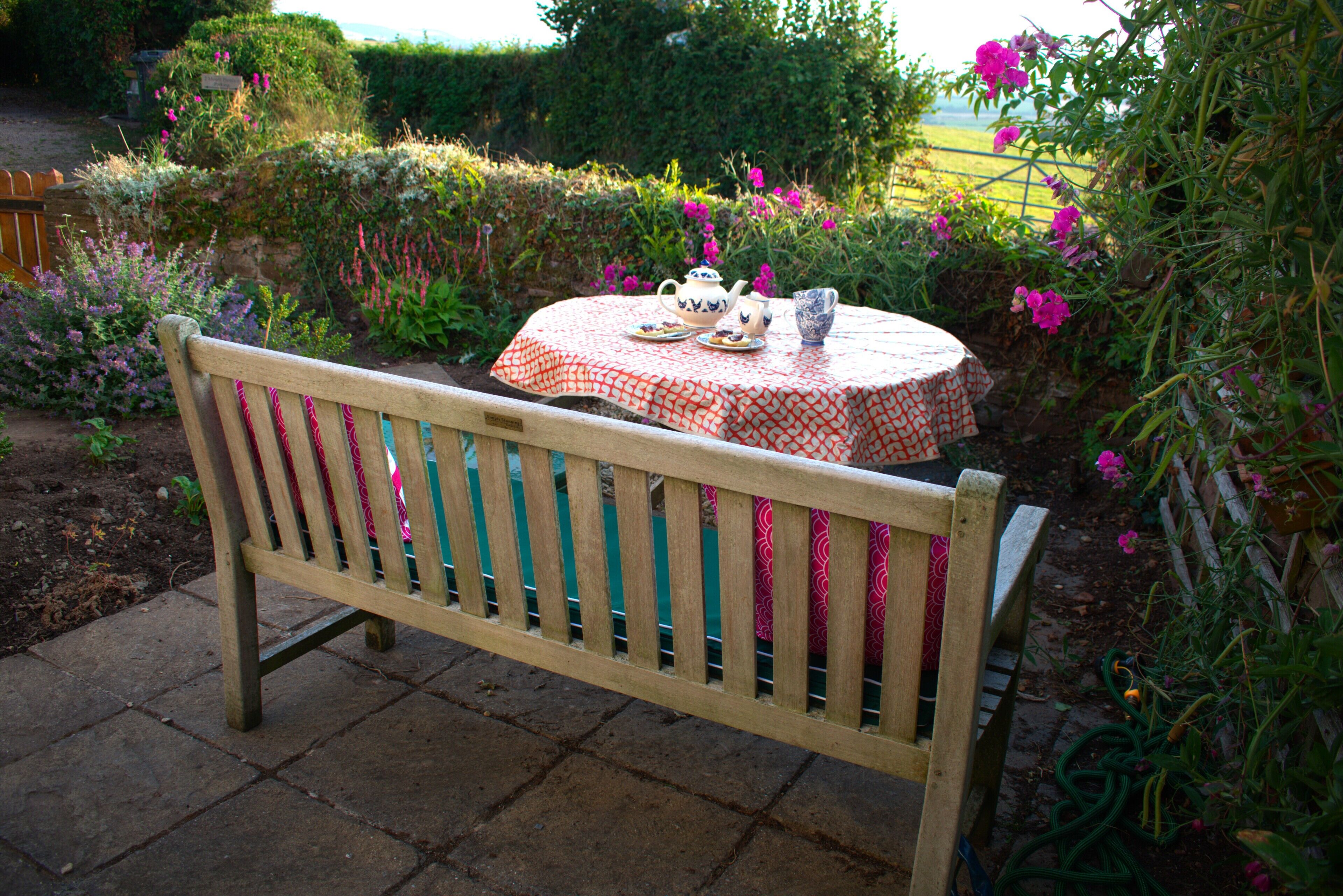 A wooden bench with a table set for tea in a garden.