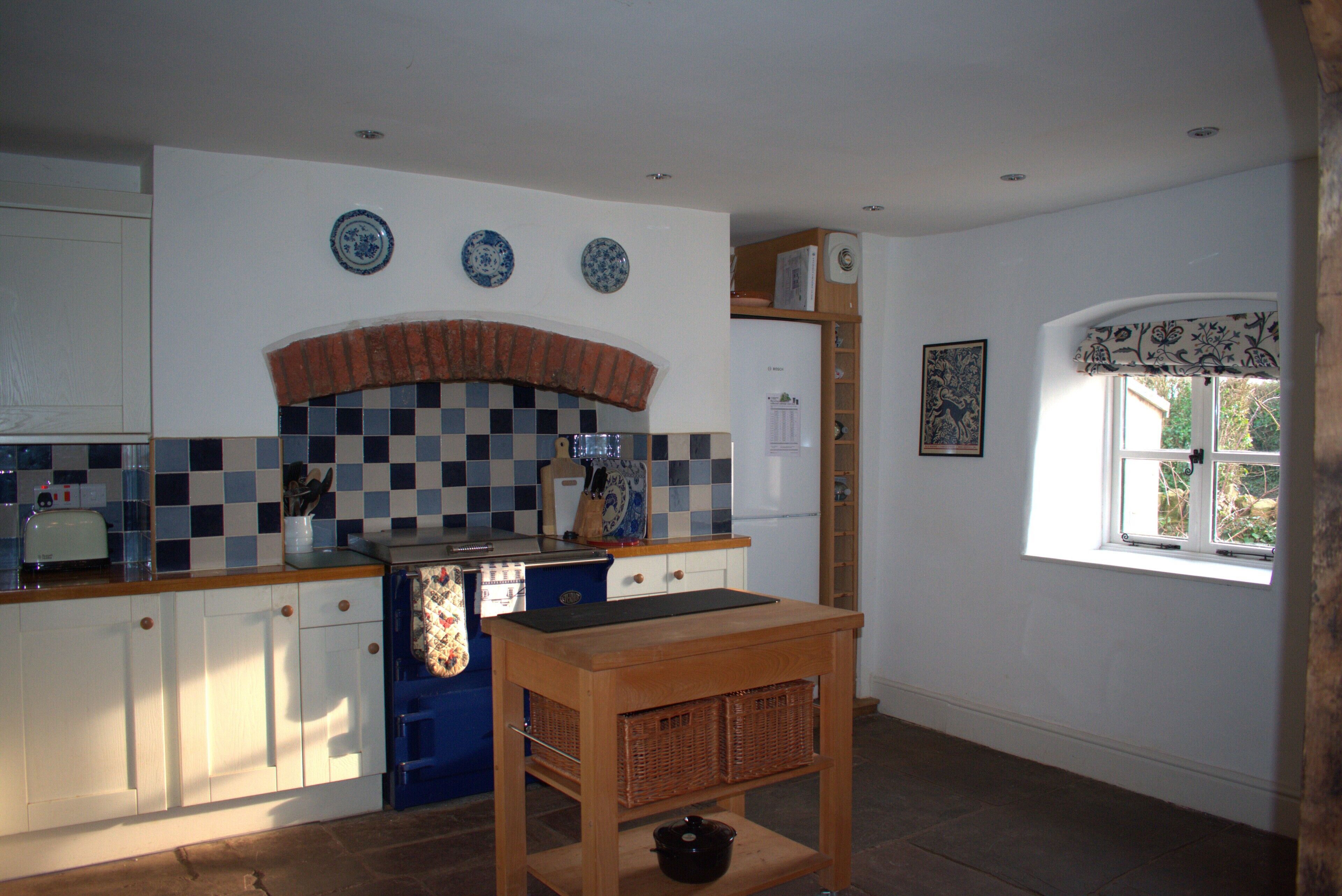 A kitchen with a tiled backsplash, a stove, and a window with a decorative valance.