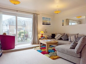 A living room with a sofa, a table, a lamp, a colorful rug, and a window with curtains. - A town house that sleeps 5 guests in 3 bedrooms (Bognor Regis)