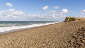 A pebbly beach with a rocky cliff and ocean waves.
