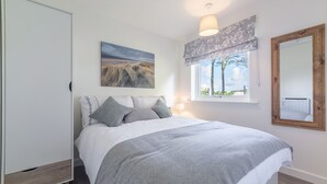 A bedroom with a bed, a window with a view, a painting on the wall, and a lamp.