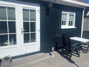Ein Haus mit einer weißen Tür, einem Fenster und einer Terrasse mit Tisch und Stühlen.