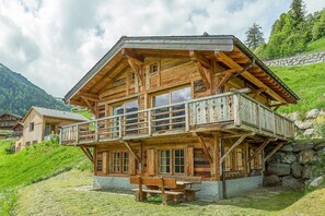 A wooden chalet with a balcony, stone foundation, and a stone wall in the background. - Chalet Jessica - La Tzoumaz, 4 Vallees (La Tzoumaz)