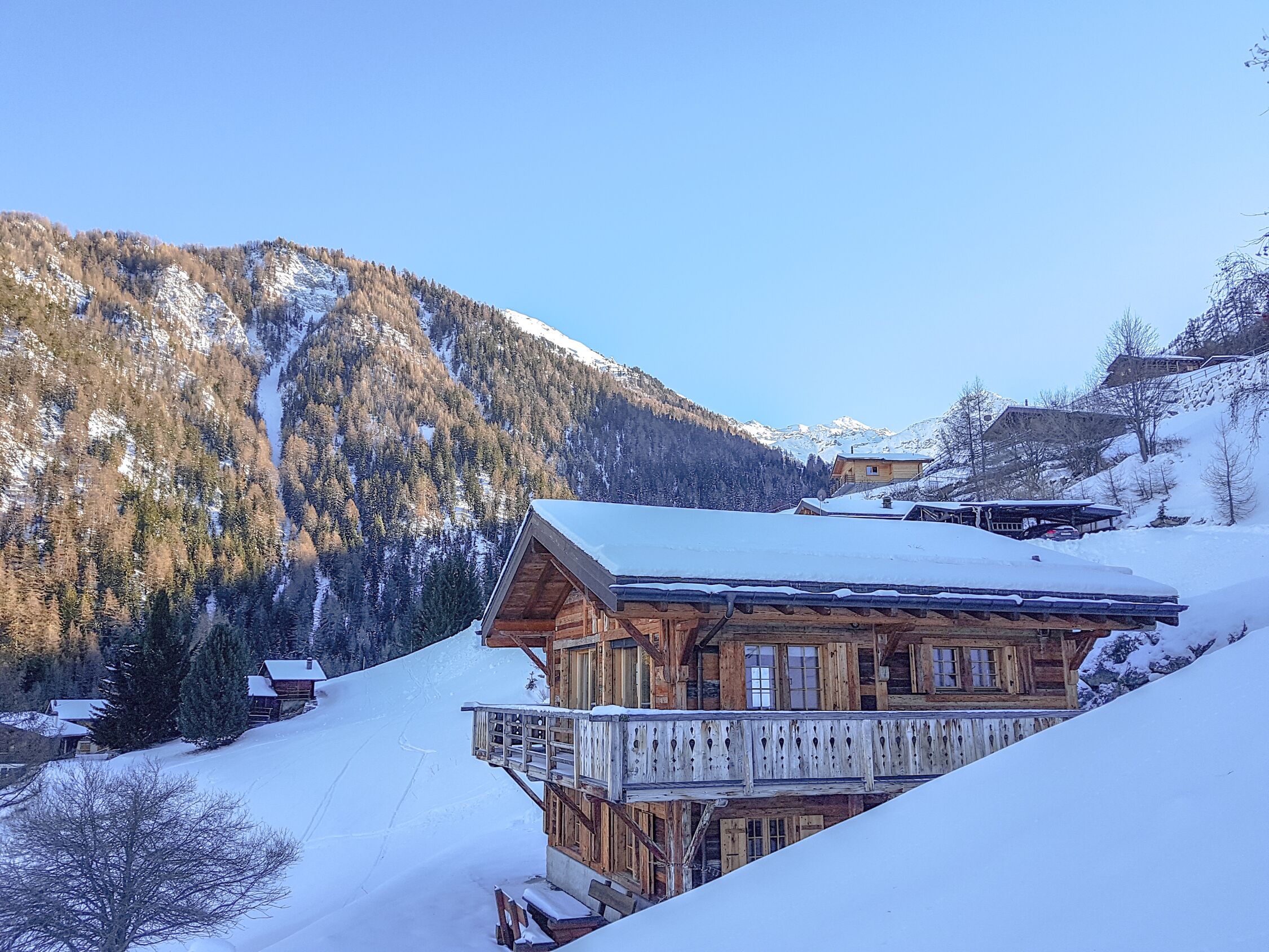 Eine Holzhütte mit Balkon, umgeben von schneebedeckten Bergen und Bäumen.