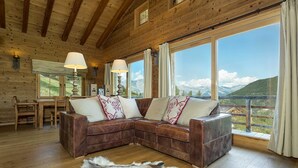 A cozy cabin interior with a wooden ceiling, a brown leather sofa with decorative pillows, a fur rug, and large windows offering a mountain view. - Chalet Jessica - La Tzoumaz, 4 Vallees (La Tzoumaz)
