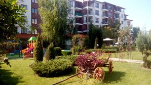 Un quartier résidentiel doté d’une aire de jeux, d’un jardin agrémenté d’un chariot décoratif et d’un immeuble à plusieurs étages avec des balcons.