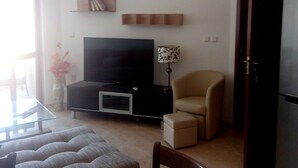 Un salon équipé d’un téléviseur à écran plat, d’un canapé, d’un fauteuil, d’une petite table et d’une lampe.