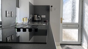 A modern kitchen with a sleek black countertop, stainless steel appliances, and a large window with frosted glass. - Traditional Croft Cottage Overlooking The Snizort River - Portree, Isle Of Skye (Portree)