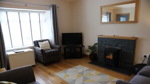 A living room with a fireplace, a flat-screen TV, and a sofa. - Traditional Croft Cottage Overlooking The Snizort River - Portree, Isle Of Skye (Portree)