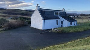 A white house with a black roof, a chimney, and a small porch. - Traditional Croft Cottage Overlooking The Snizort River - Portree, Isle Of Skye (Portree)