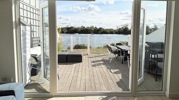 A modern interior with a large sliding glass door leading to an outdoor deck with a view of a lake. - BOOK NOW ON LINE (Cirencester)