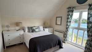 A bedroom with a bed, nightstands, a window with curtains, and a view of the outdoors. - BOOK NOW ON LINE (Cirencester)