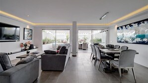 Un salon moderne avec un canapé gris, une table à manger avec des chaises et une grande fenêtre donnant sur l’extérieur.