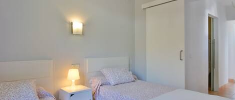 A bedroom with two beds, a nightstand with a lamp, a wall-mounted light, and a sliding door closet.