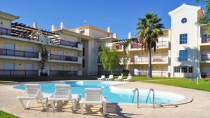 A pool area with lounge chairs and a clear blue pool, surrounded by multi-story buildings with balconies. - Flat Bogart OCV - Oura Albufeira (Albufeira)