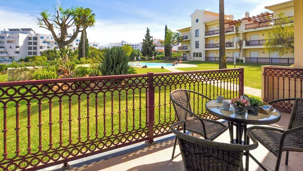 A balcony with wicker chairs and a table, overlooking a swimming pool and a well-maintained lawn. - Flat Bogart OCV - Oura Albufeira (Albufeira)