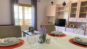 A dining area with a table set for four, including plates, glasses, and cutlery. There is a television on a stand in the background, and a cabinet with glass doors to the right. - Flat Bogart OCV - Oura Albufeira (Albufeira)