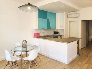 A modern kitchen with a central island, white cabinetry, a teal accent wall, and a glass dining table with white chairs.