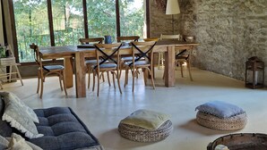 Un interior rústico con pared de piedra, mobiliario de madera y amplios ventanales que dan a vistas de vegetación.