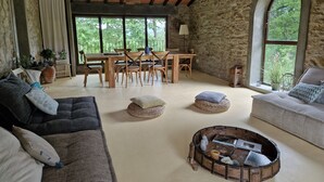 Una habitación acogedora con pared de piedra, muebles de madera y ventanas amplias que dan a zonas verdes.