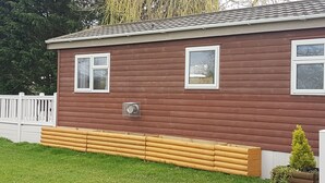 Ein eingeschossiges Holzhaus mit zwei Fenstern, einer kleinen Veranda und einem weißen Zaun im Hintergrund.