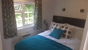 Ein Schlafzimmer mit Bett, Vorhängen, Heizkörper und Fenster mit Blick ins Grüne.