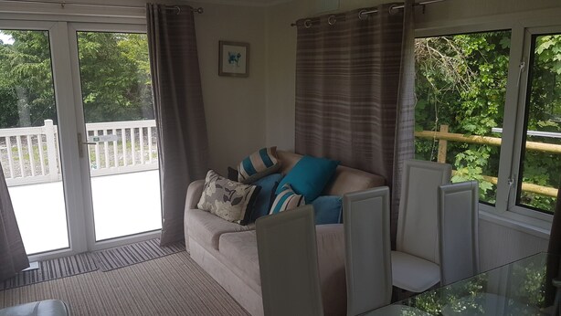 Ein Zimmer mit einer Couch, einem Glastisch und Blick auf einen Balkon und grüne Bepflanzung.