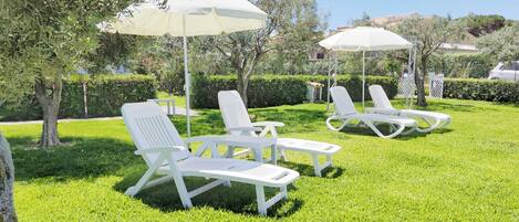 A well-maintained outdoor seating area with white lounge chairs and umbrellas, surrounded by neatly trimmed hedges and trees.