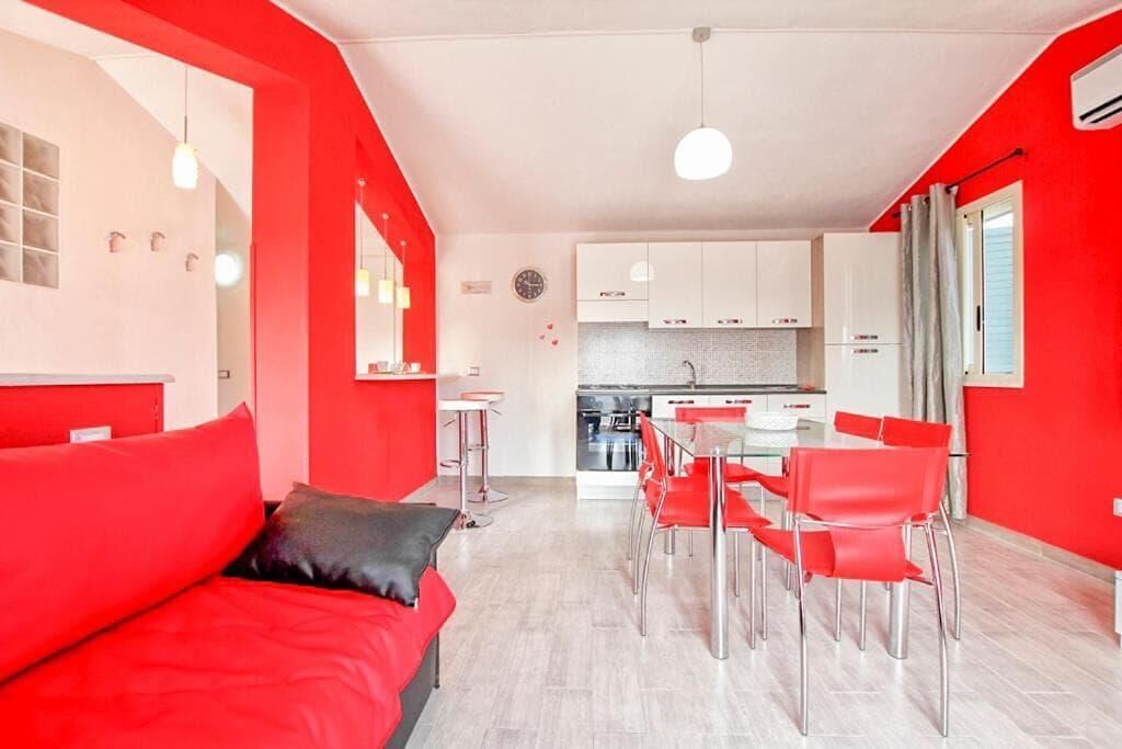 A modern living room with red furniture, a dining area with red chairs, and a kitchen in the background.
