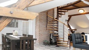 Un comedor con una mesa y sillas de madera, una pared de ladrillo y una escalera en espiral.