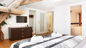 Un dormitorio moderno con una cama grande, un aparador de madera oscura, un televisor de pantalla plana y un detalle decorativo en el techo de madera.