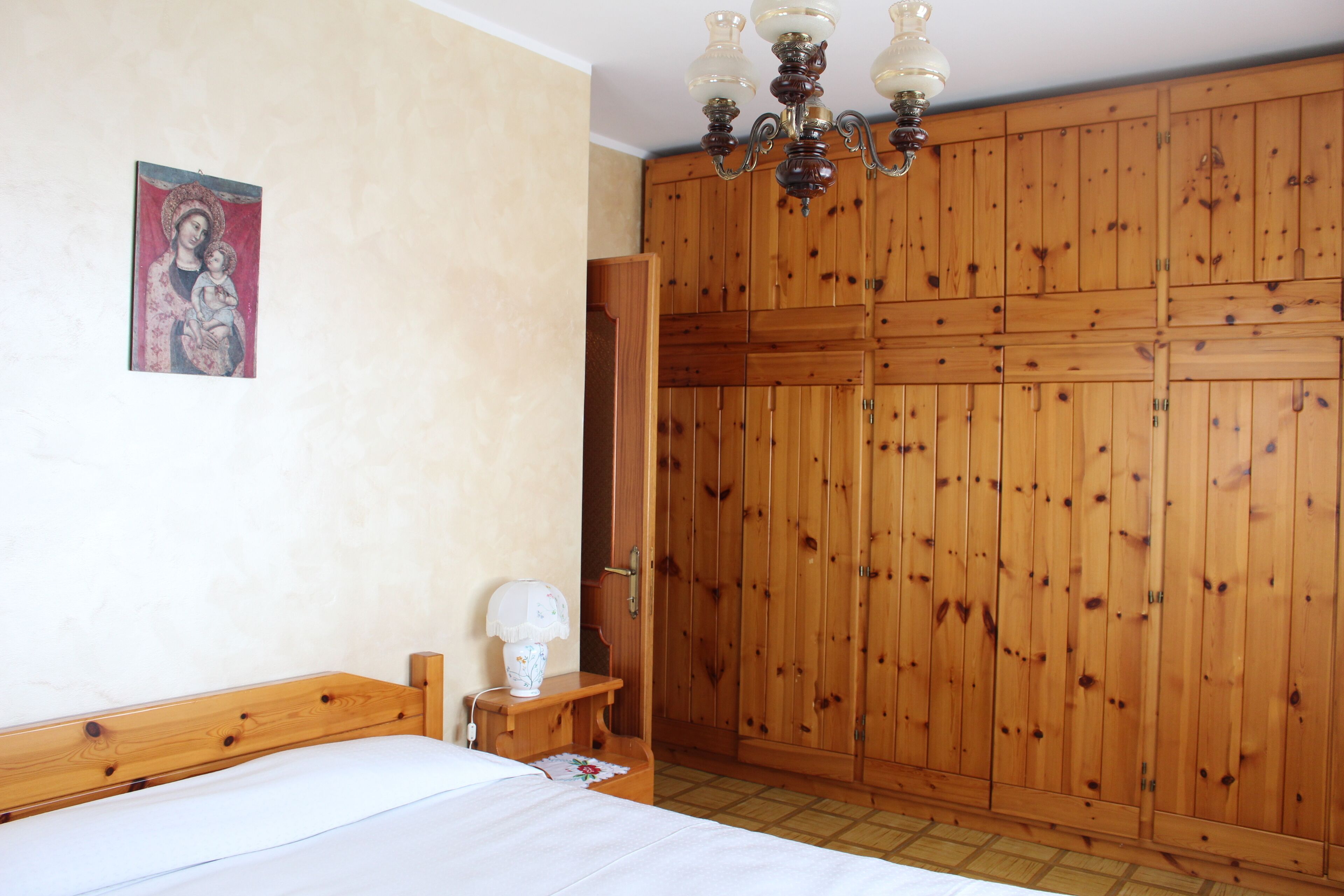 Ein Schlafzimmer mit Holzschrank, Bett, Nachttisch und Wandlampe.