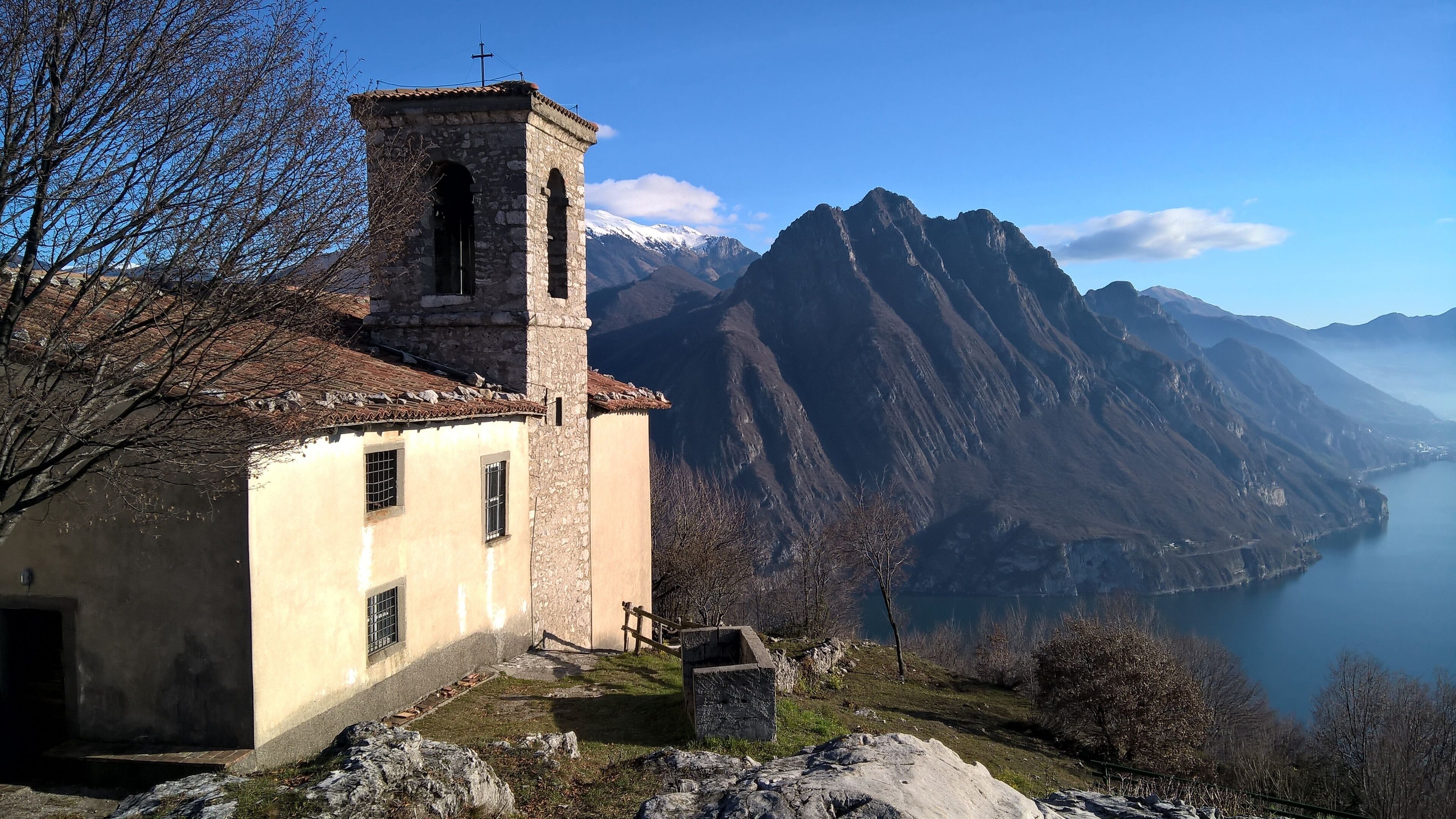 A stone church with a bell tower, a small bell, and a stone wall.