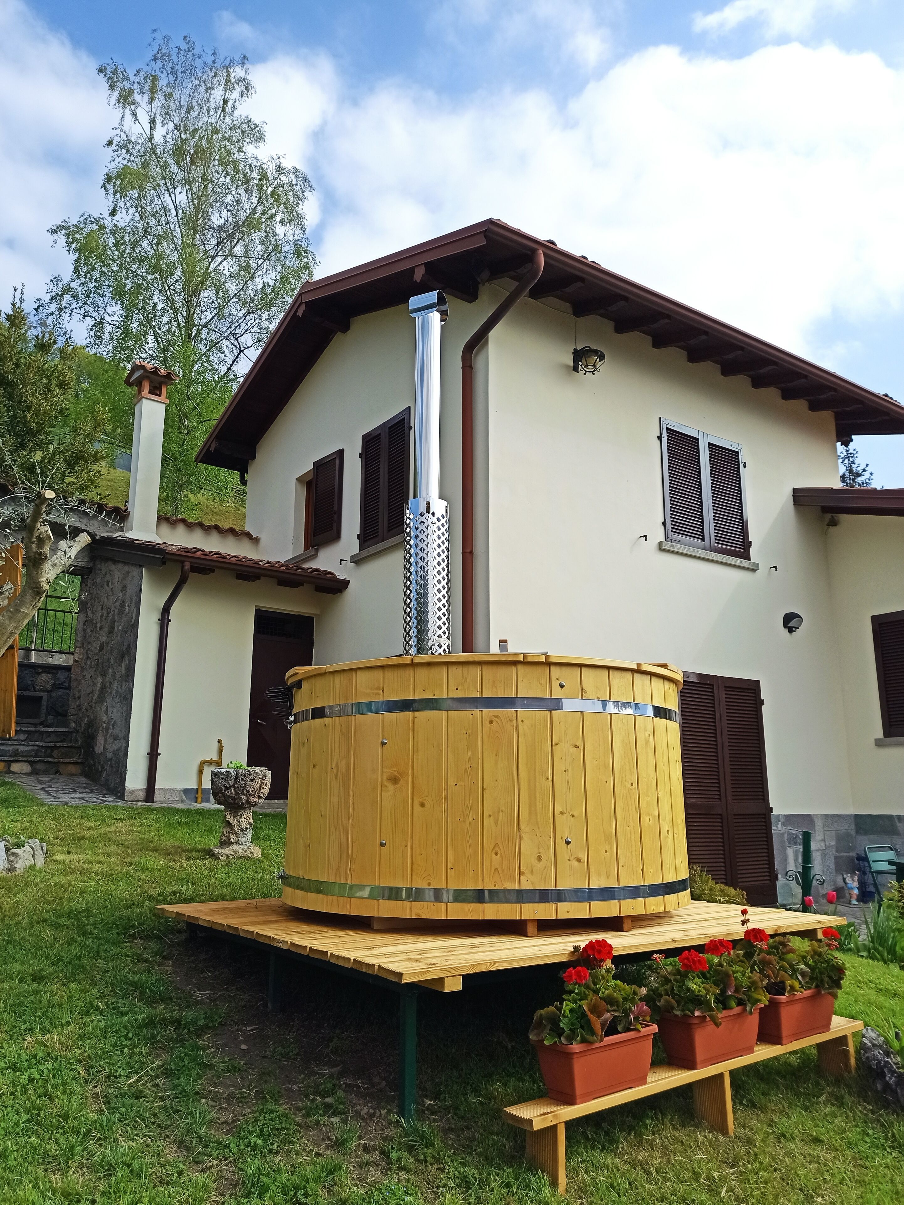 A house with a wooden sauna, a stone fountain, and a garden with potted plants.