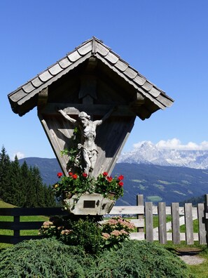 A wooden structure with a crucifix, surrounded by greenery and flowers, with a mountain backdrop. - Large, Centrally Located Apartment (Altenmarkt im Pongau)