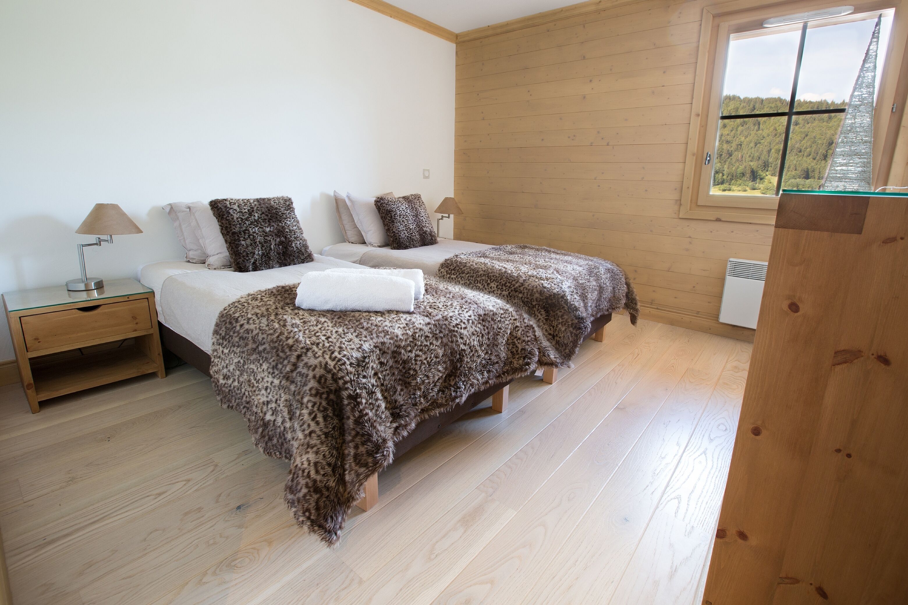 Une chambre avec deux lits, un plancher en bois, une fenêtre avec vue et une table de chevet avec une lampe.