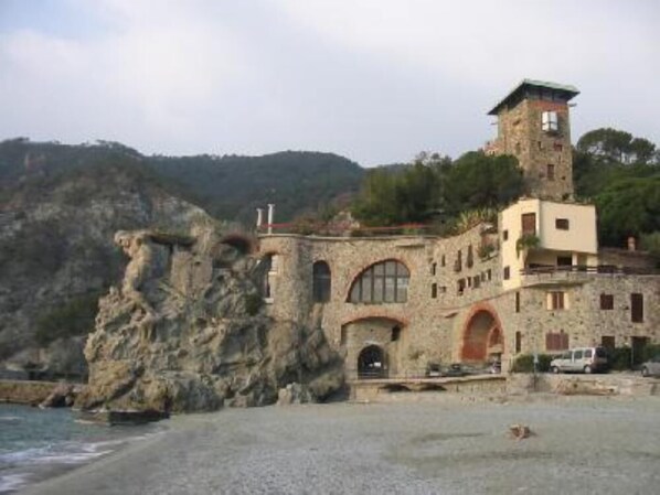 A coastal building with a tower, stone walls, and a beach in the foreground.